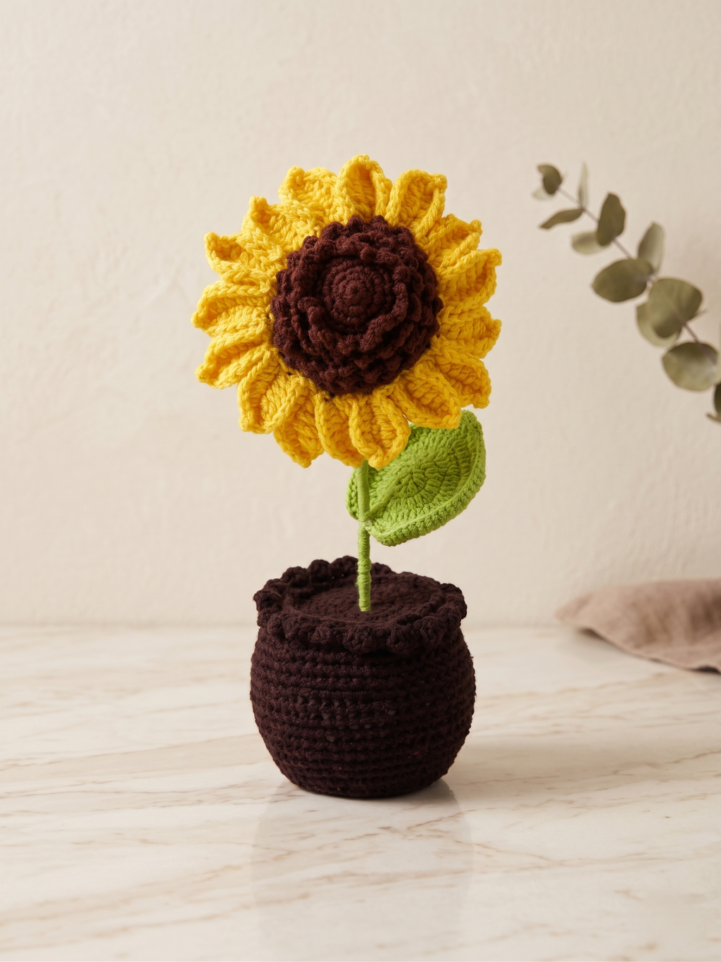 Crochet sunflower in a dark pot, standing on a pale surface
