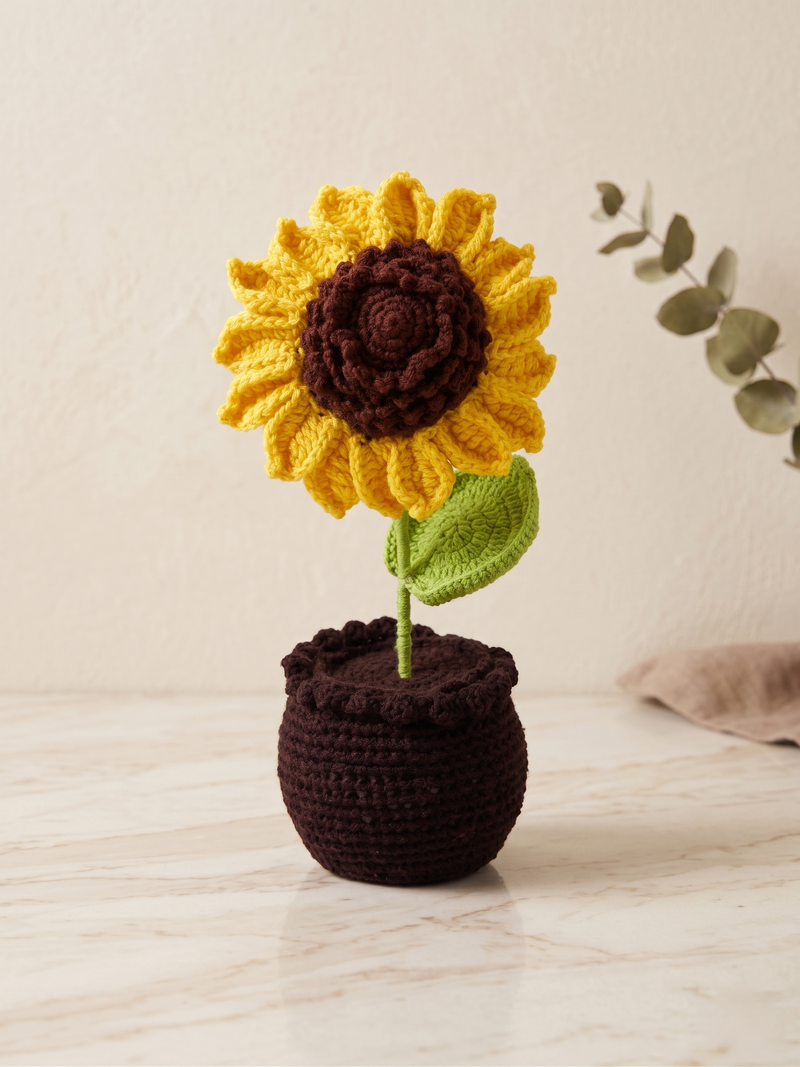 Crochet sunflower in a dark pot, standing on a pale surface